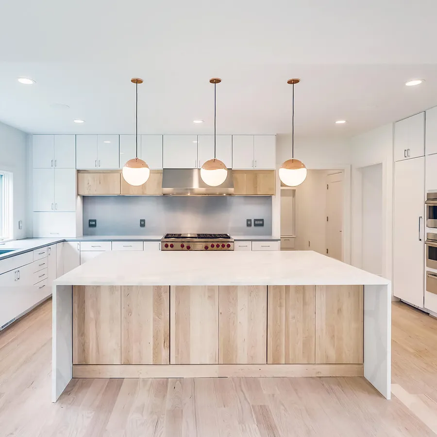 White kitchen with light wood island, waterfall stone countertop and globe pendants