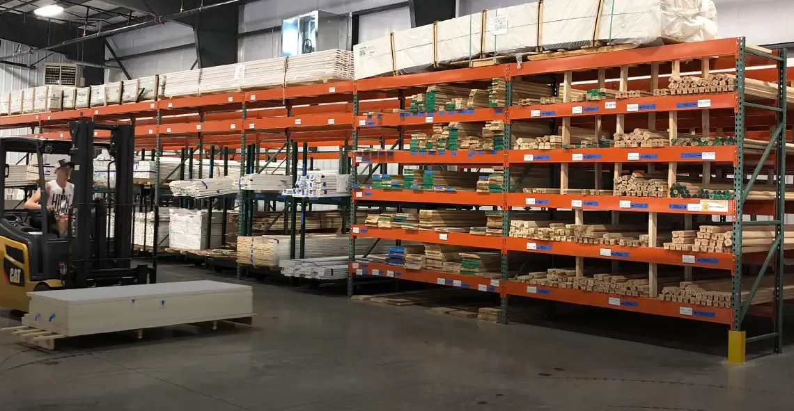 Orange warehouse racks stocked with bundled moulding beside a forklift