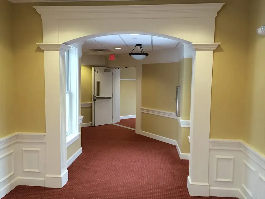 Arched hallway opening with white columns, crown trim, and paneled wainscoting
