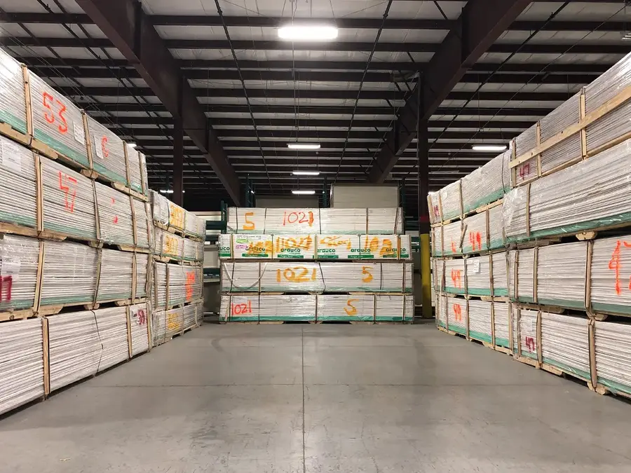 Warehouse aisle lined with tall stacks of bundled white boards on pallets