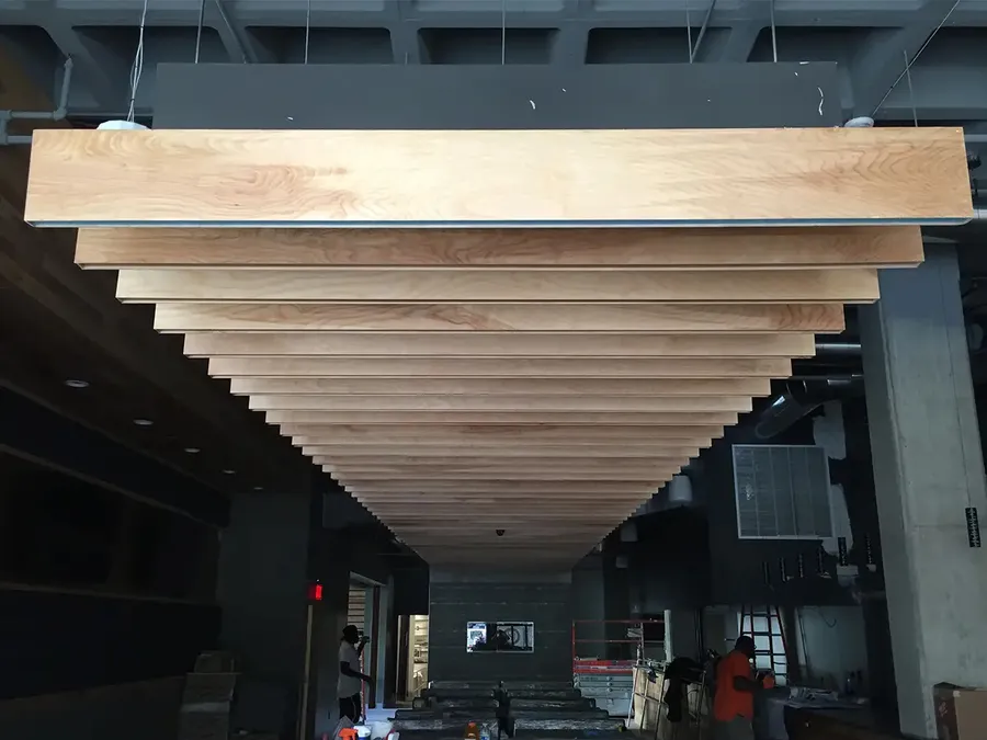 Tiered wood-clad ceiling baffles suspended in a commercial space under construction