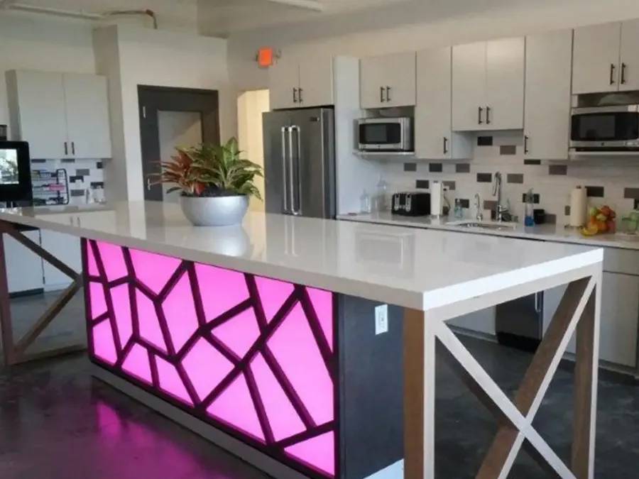 Office kitchen island with a backlit pink geometric panel and X-braced wood legs