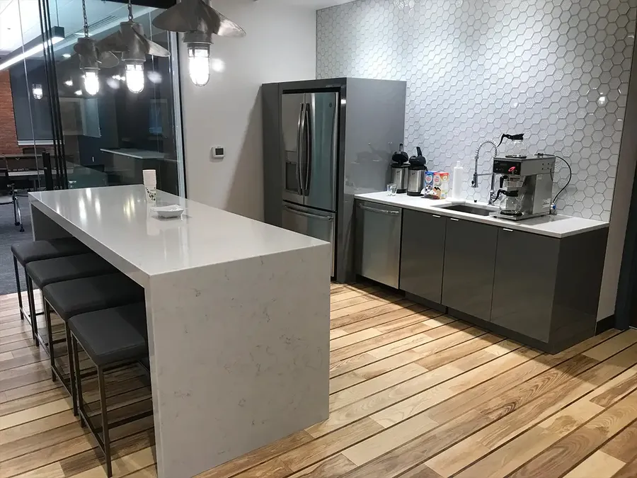 Office kitchen with a waterfall stone island, gray gloss cabinets, and hexagon tile