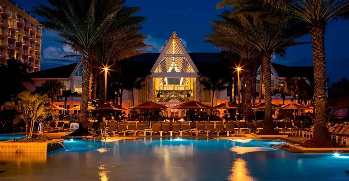 Resort pool at night lit by lamps, with palm trees and lounge chairs