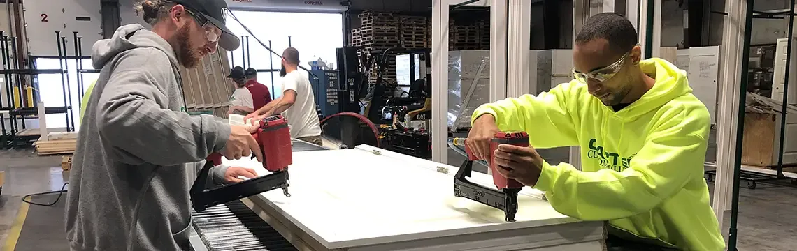 Two workers using staple guns to assemble a door unit on a workbench