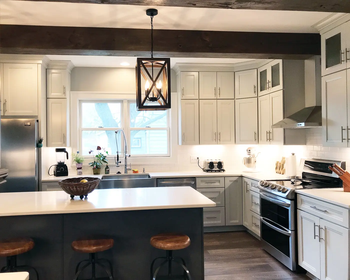 White kitchen with dark island, wood ceiling beams and black lantern pendant