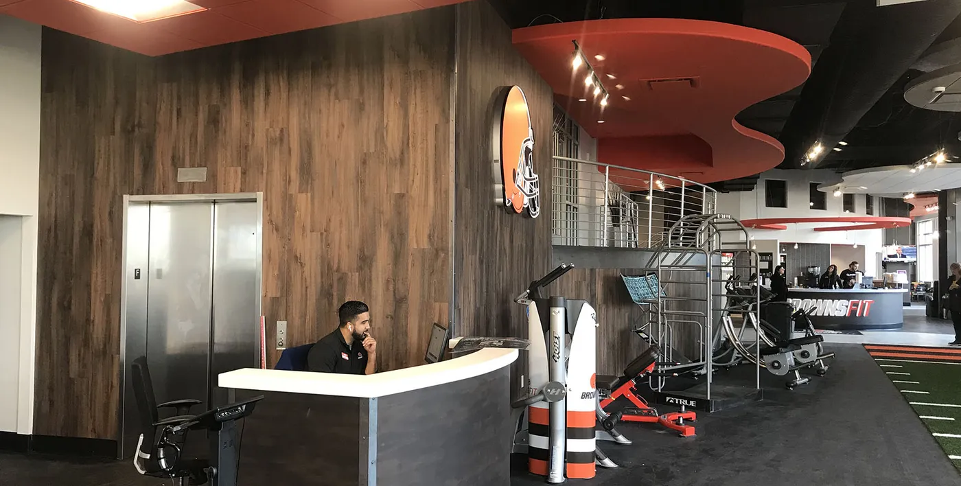 Fitness center lobby with wood-grain wall panels, reception desk and Browns helmet sign
