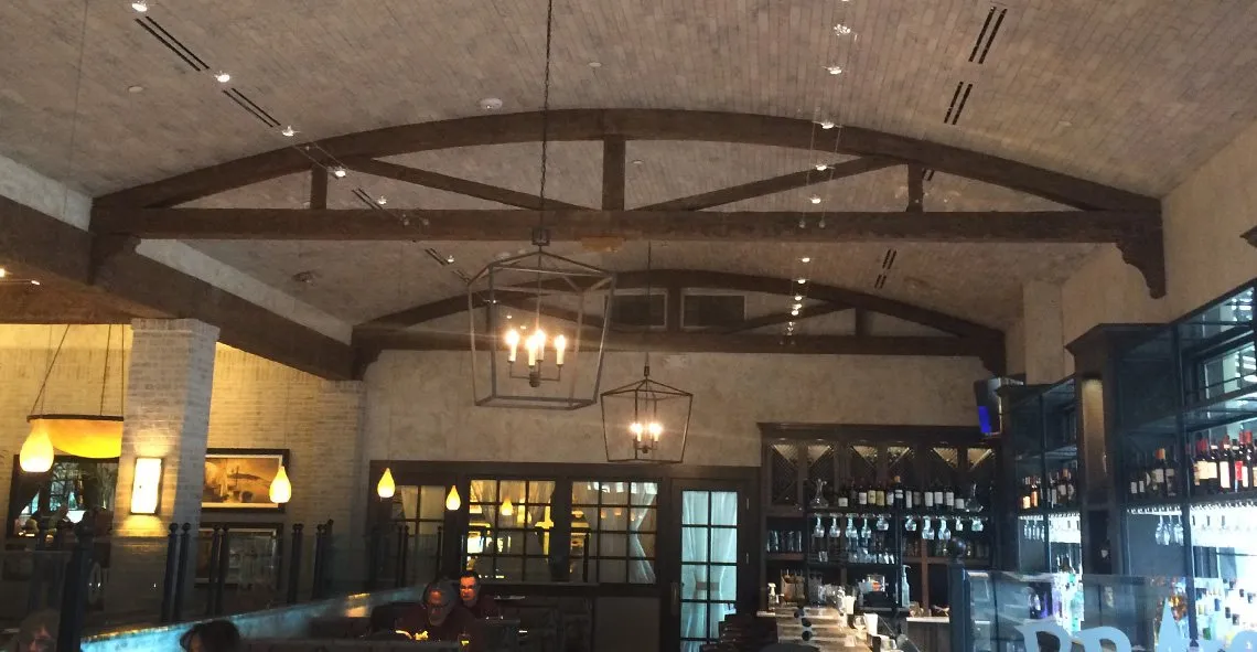 Restaurant with dark timber arched beams under a barrel brick ceiling and lantern pendants