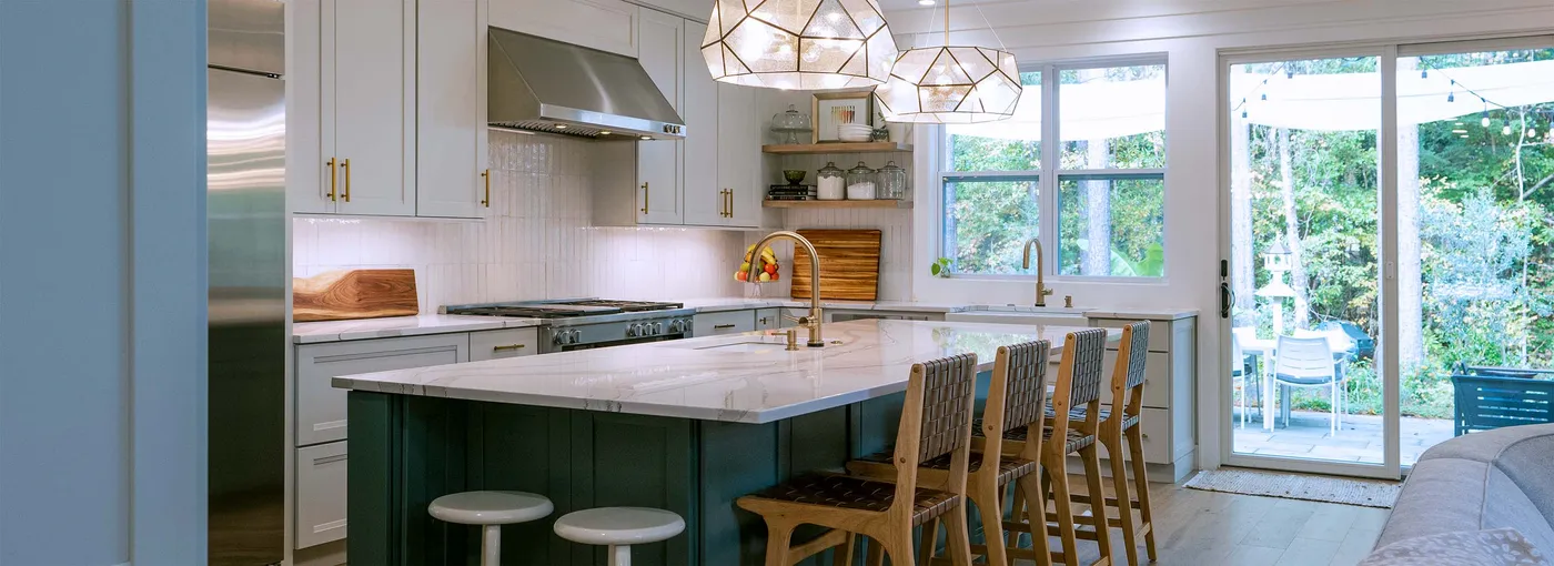 White kitchen with teal island, woven stools and geometric pendants beside patio doors