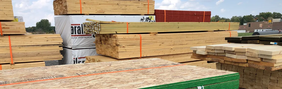 Stacks of dimensional lumber, plywood and wrapped bundles in an outdoor lumber yard