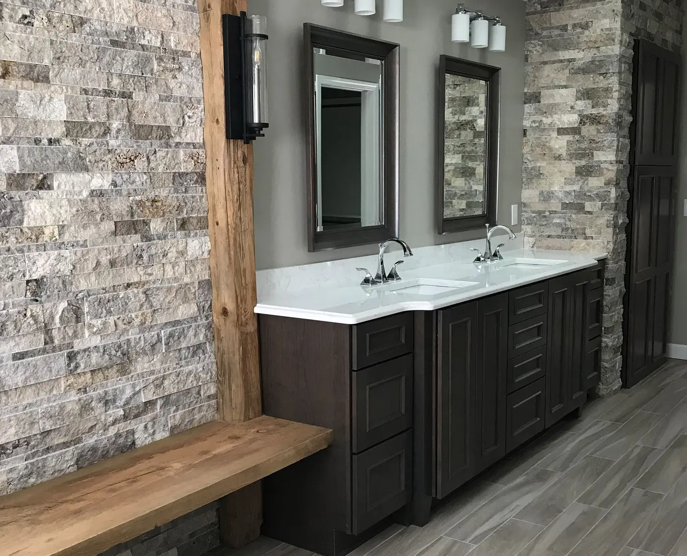 Bathroom with dark double vanity, stacked stone walls, wood post and wood bench
