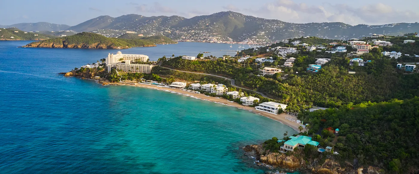 Aerial view of a beachfront resort on a turquoise bay with green hills